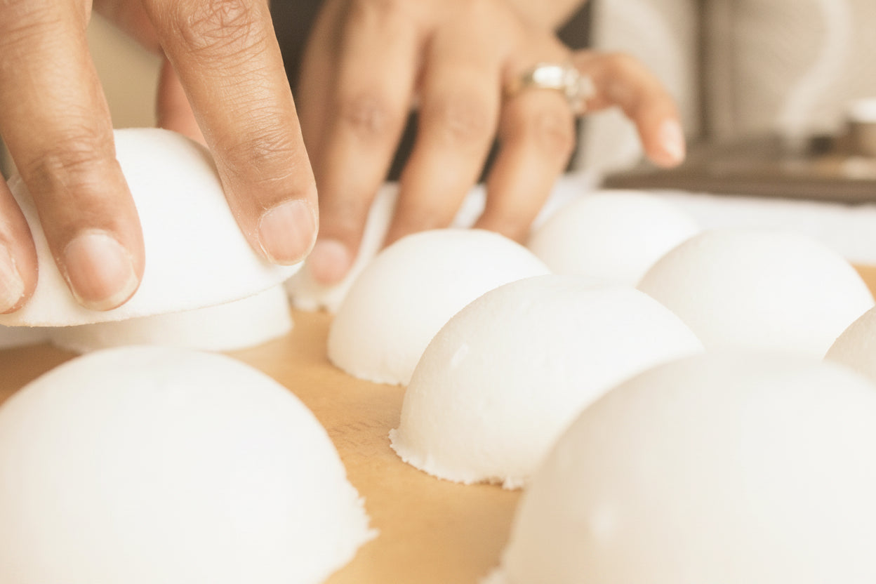 Hands arranging white spherical objects on a surface with a blurred background