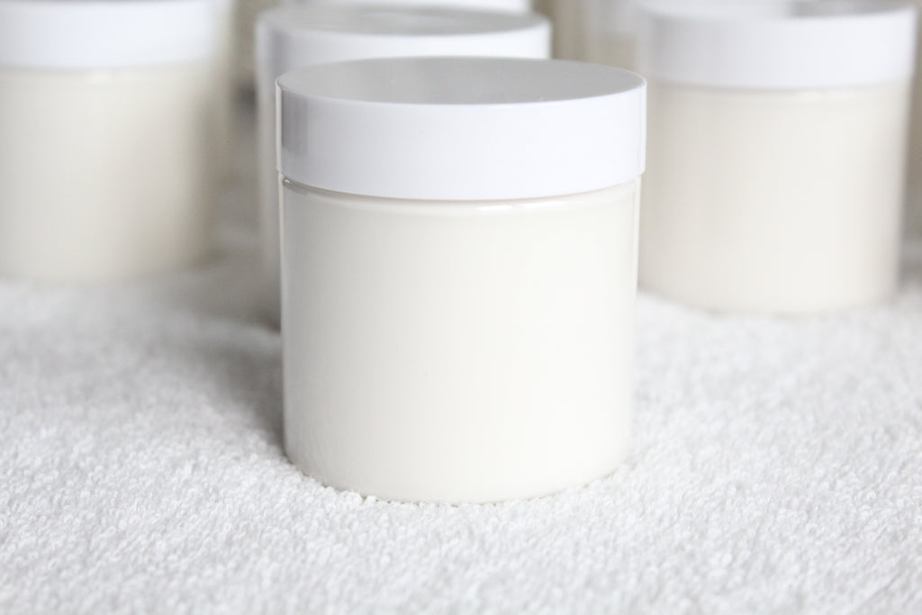 White cylindrical containers of body butter by Busy Little Body on a textured white surface