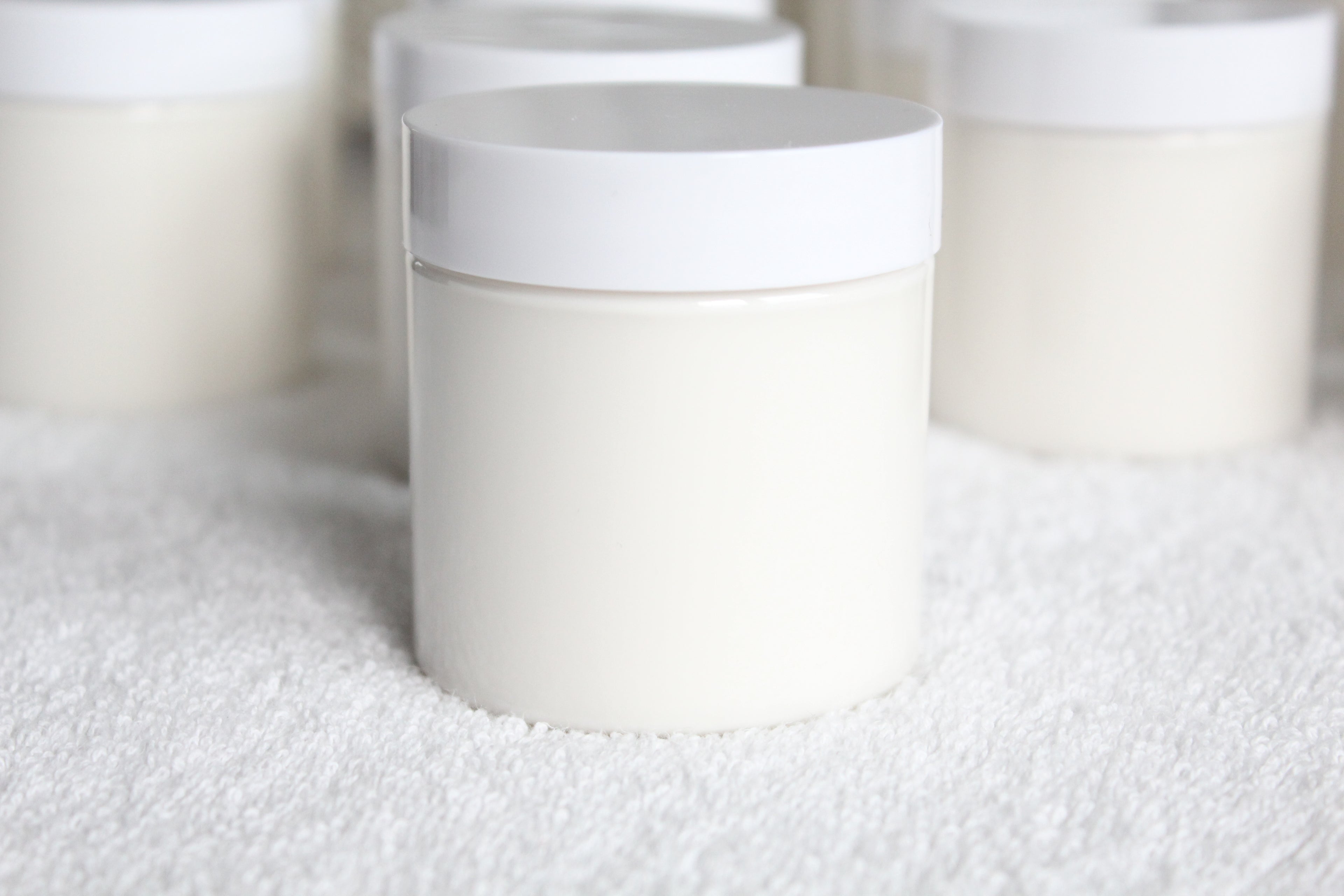White cylindrical containers of body butter by Busy Little Body on a textured white surface