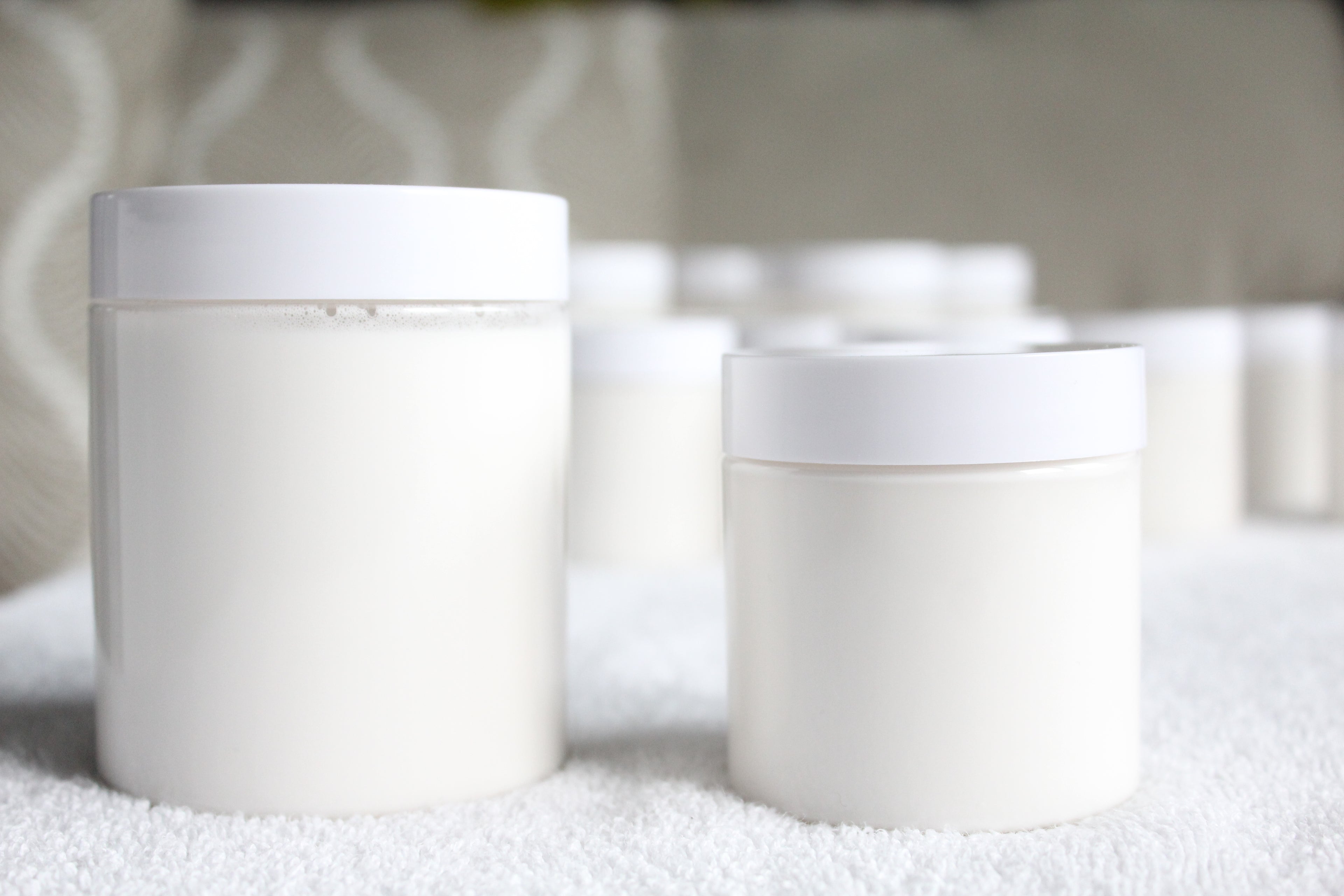 Two white plastic containers of body butter by Busy Little Body on a textured surface with a blurred background