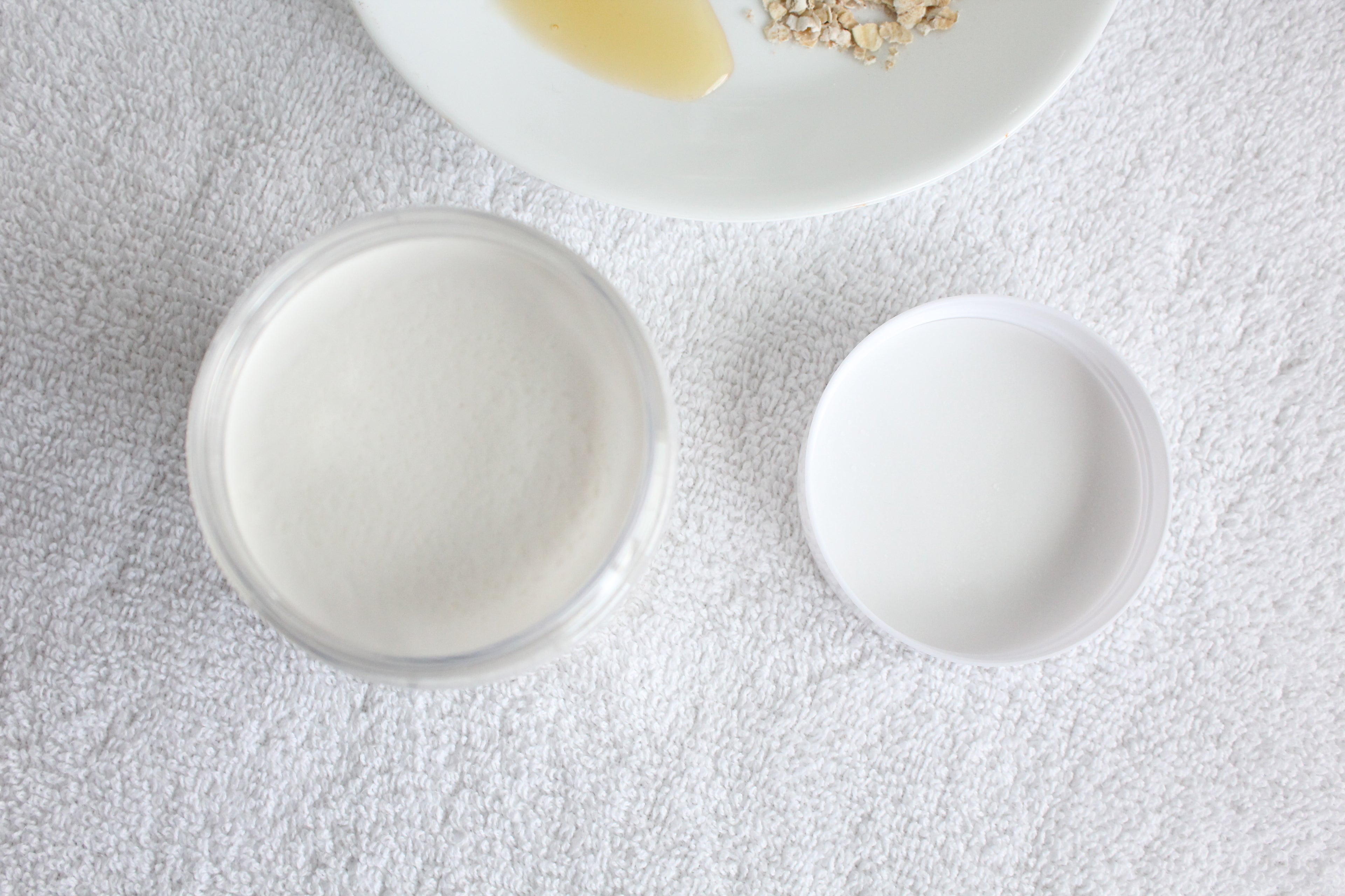 Two white body butter jars on a textured gray surface.
