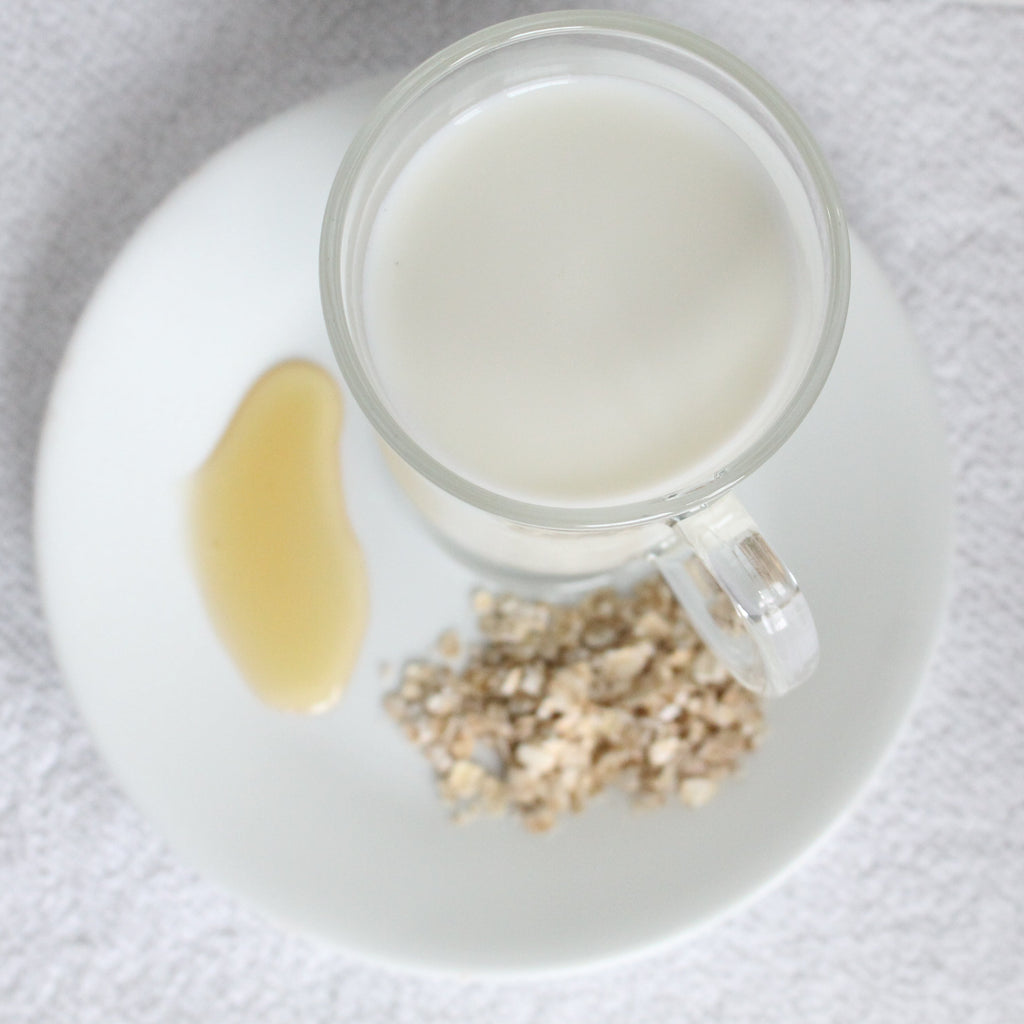 Glass of milk with honey and oats on a white plate