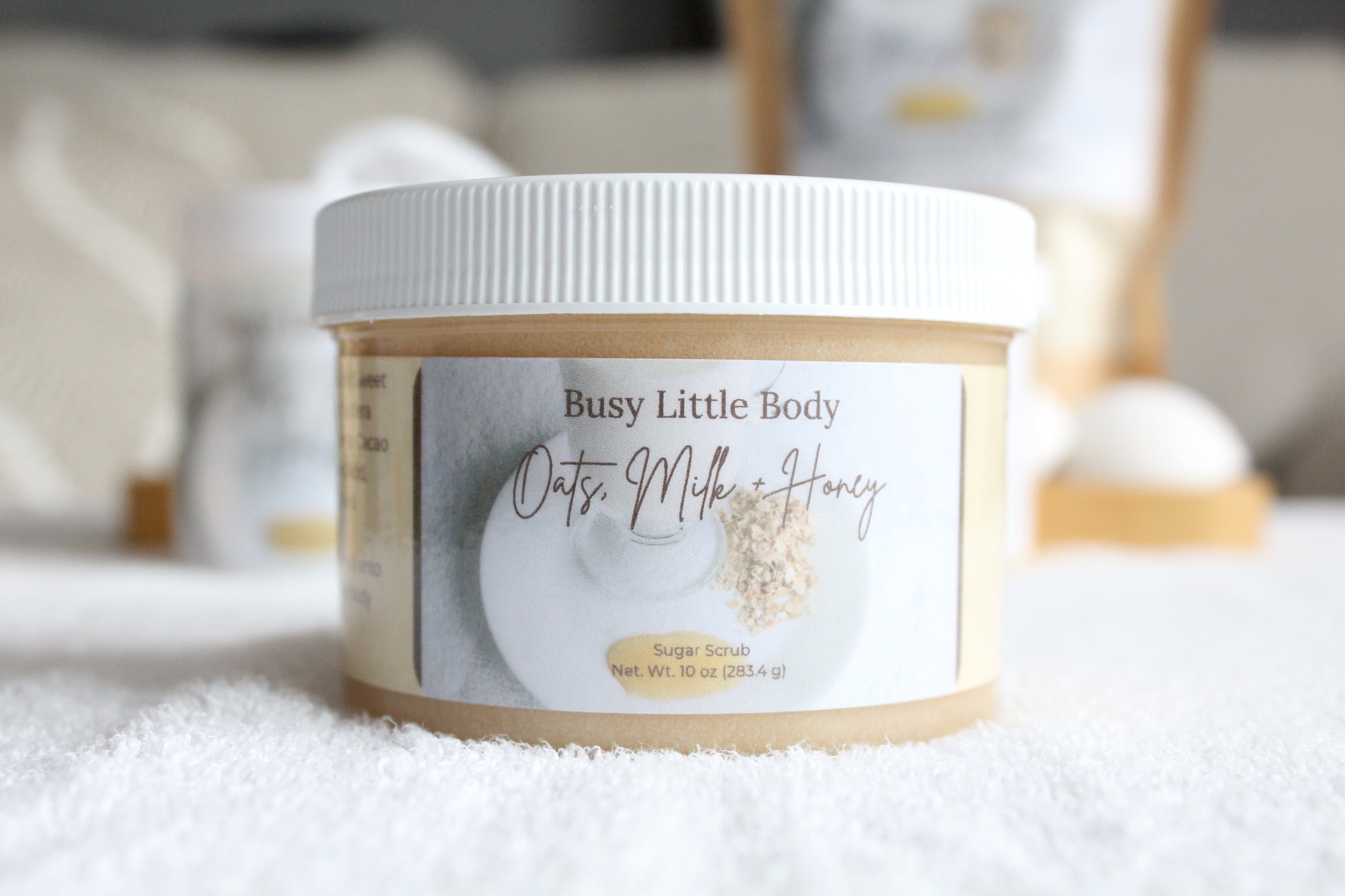 Jar of 'Oats Milk & Honey' sugar scrub by 'Busy Little Body' on a white surface.