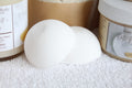 White bath bomb on a white surface with product containers in the background