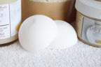 White bath bomb on a white surface with product containers in the background