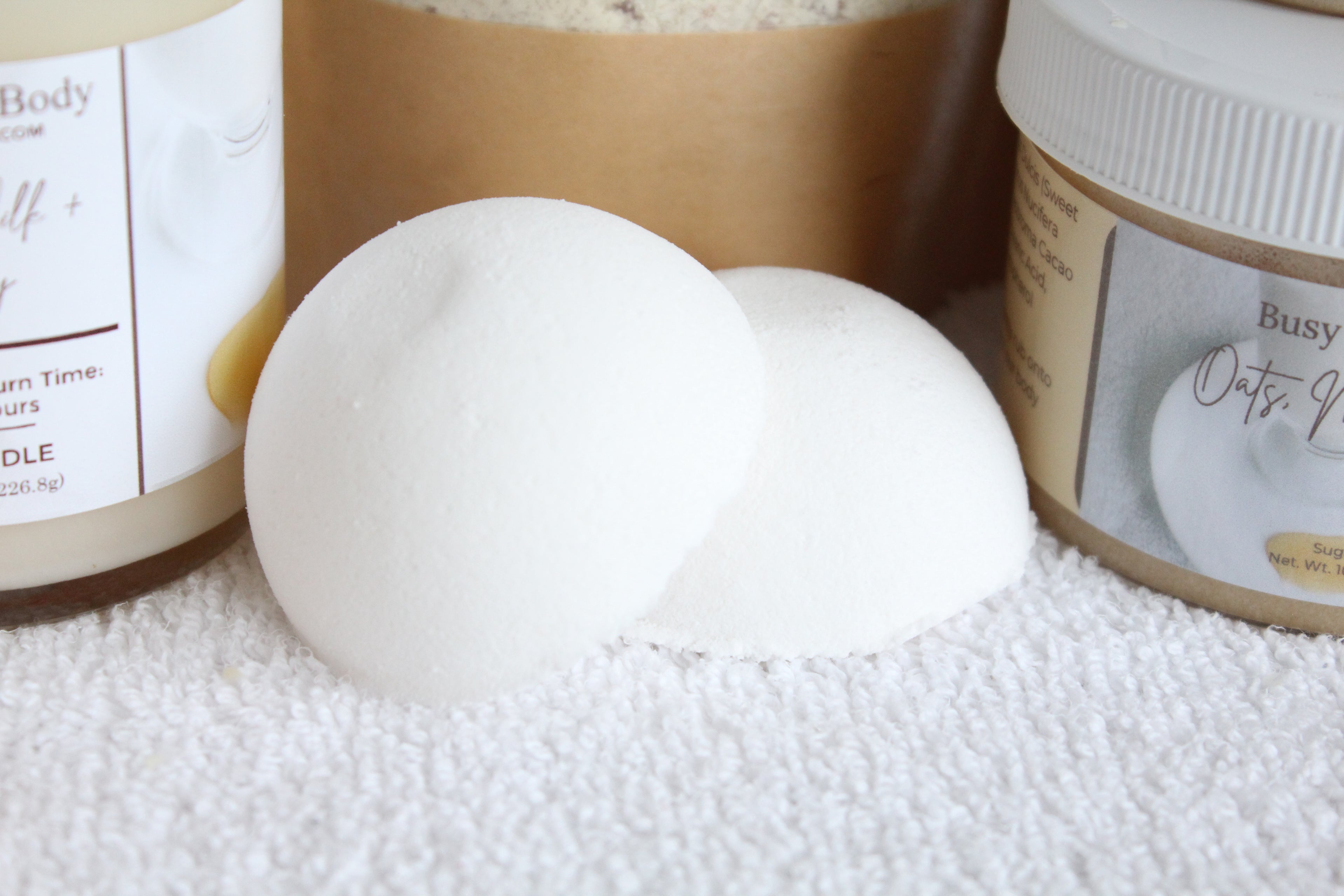 White bath bomb on a white surface with product containers in the background