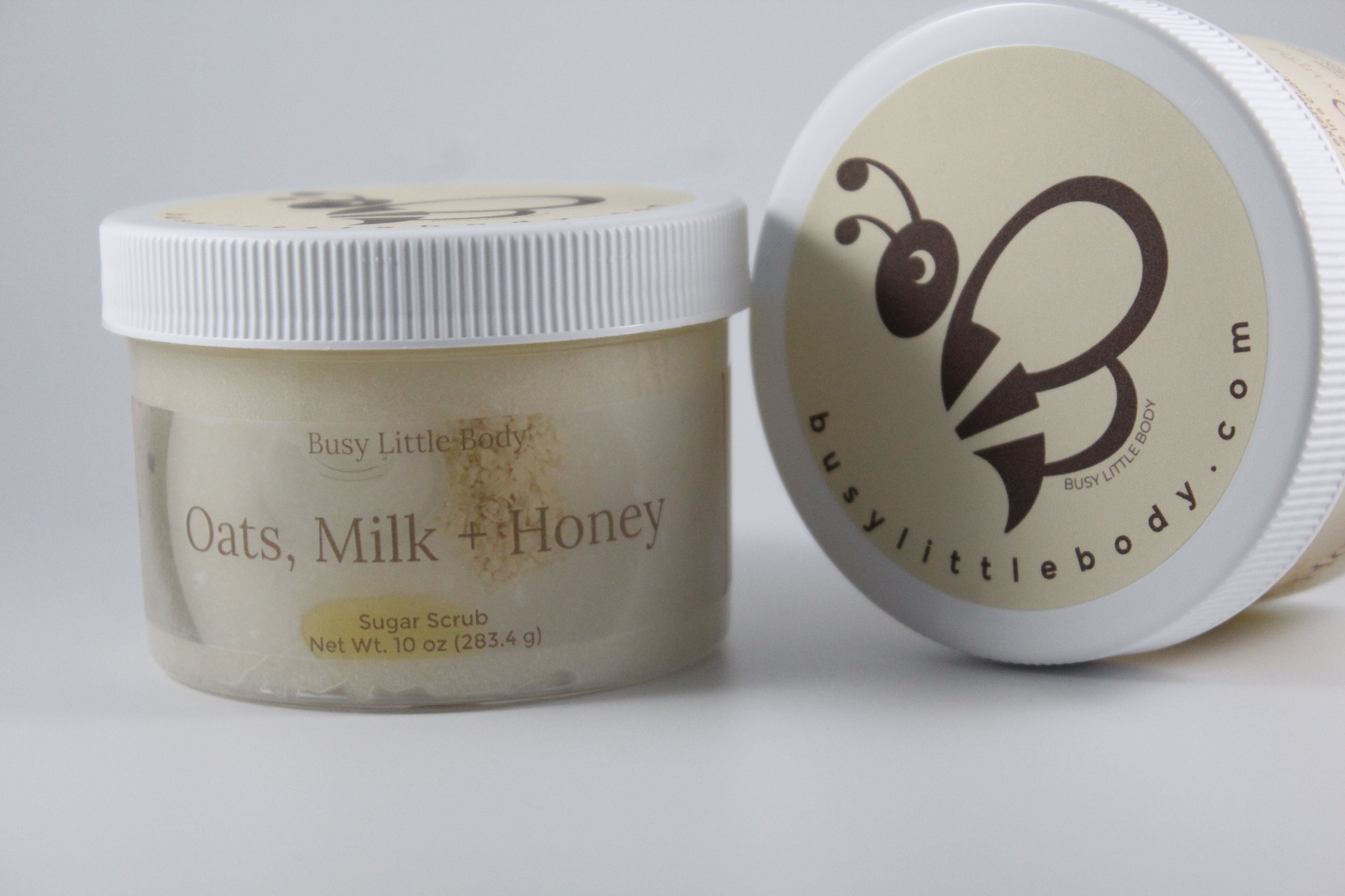 Jar of 'Oats, Milk + Honey' sugar scrub with a visible brand logo on a light background