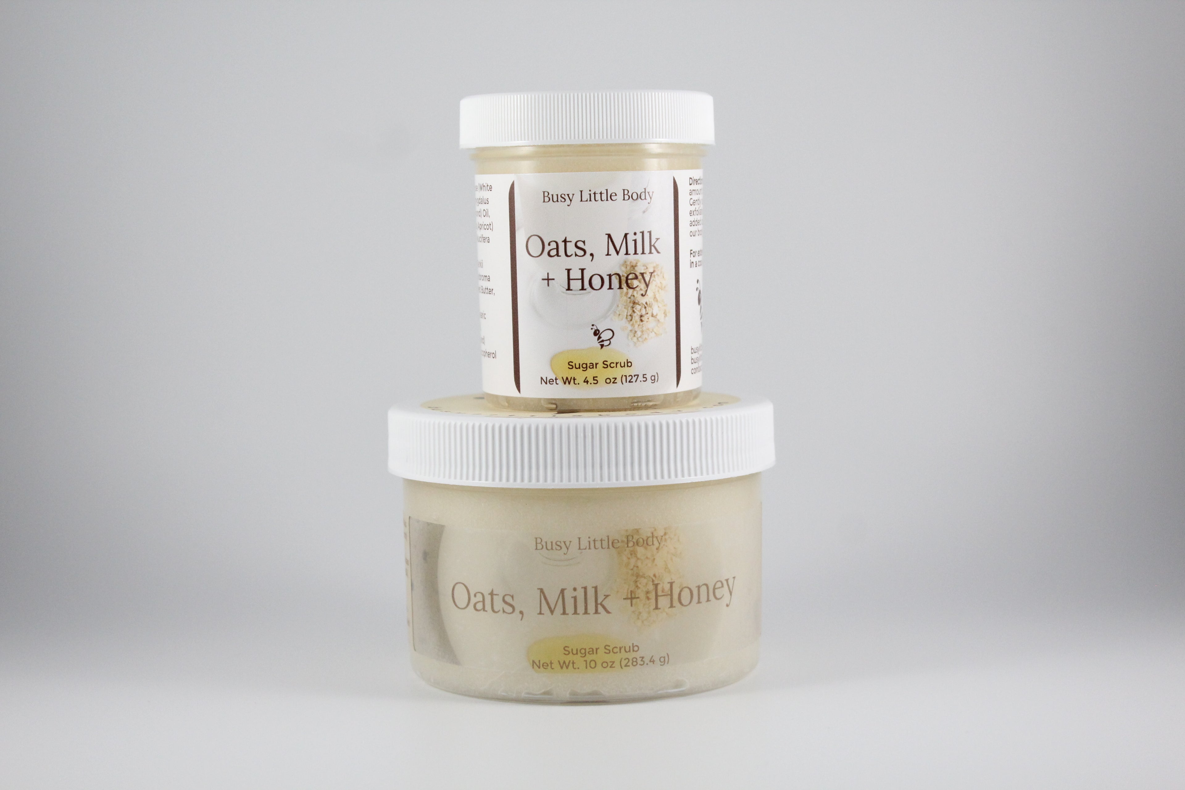 Two jars of 'Oats, Milk + Honey' body product on a gray background