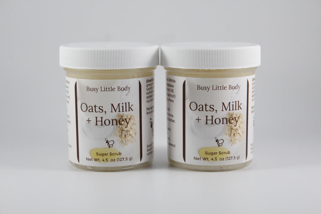 Two jars of 'Oats, Milk + Honey' sugar scrub by Busy Little Body on a gray background.