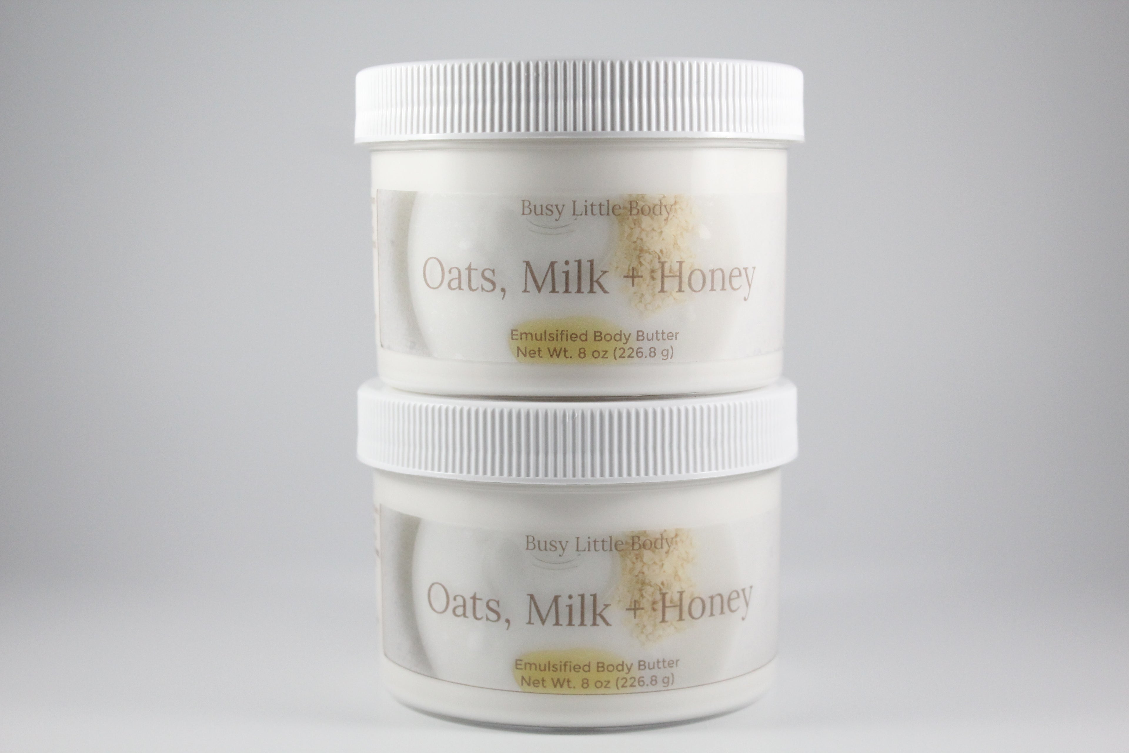 Two containers of Busy Little Body Oats, Milk + Honey body butter on a gray background