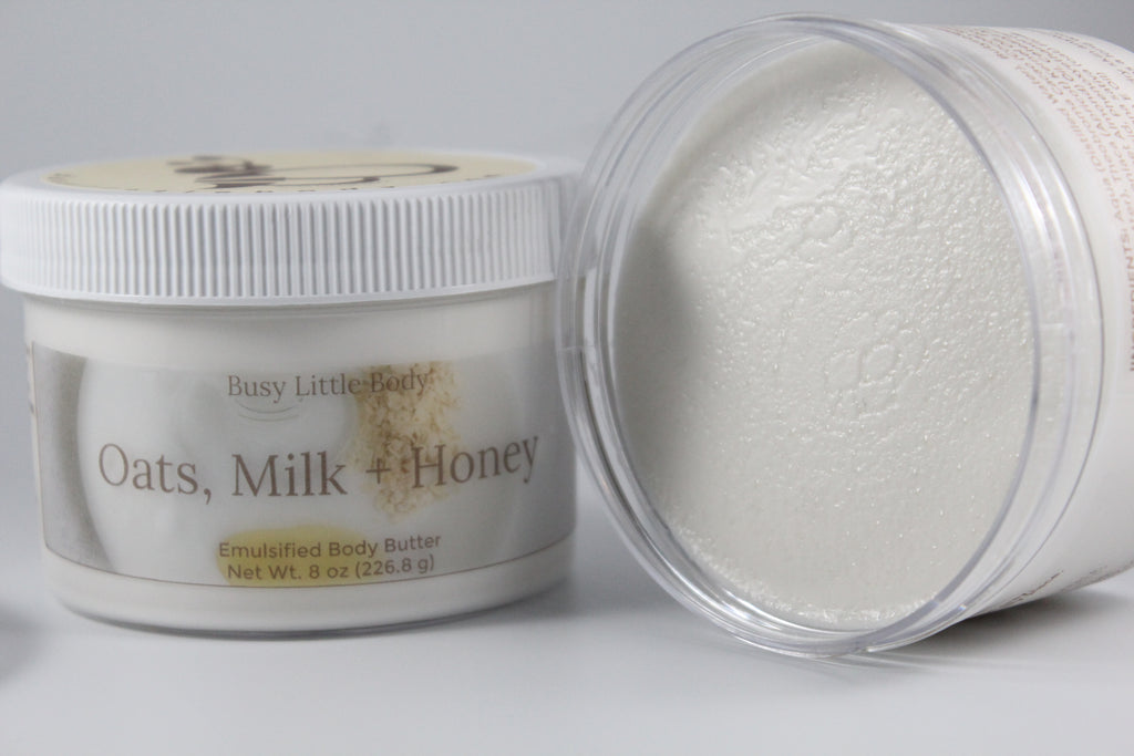Body butter container labeled 'Oats, Milk + Honey' by Busy Little Body on a gray background