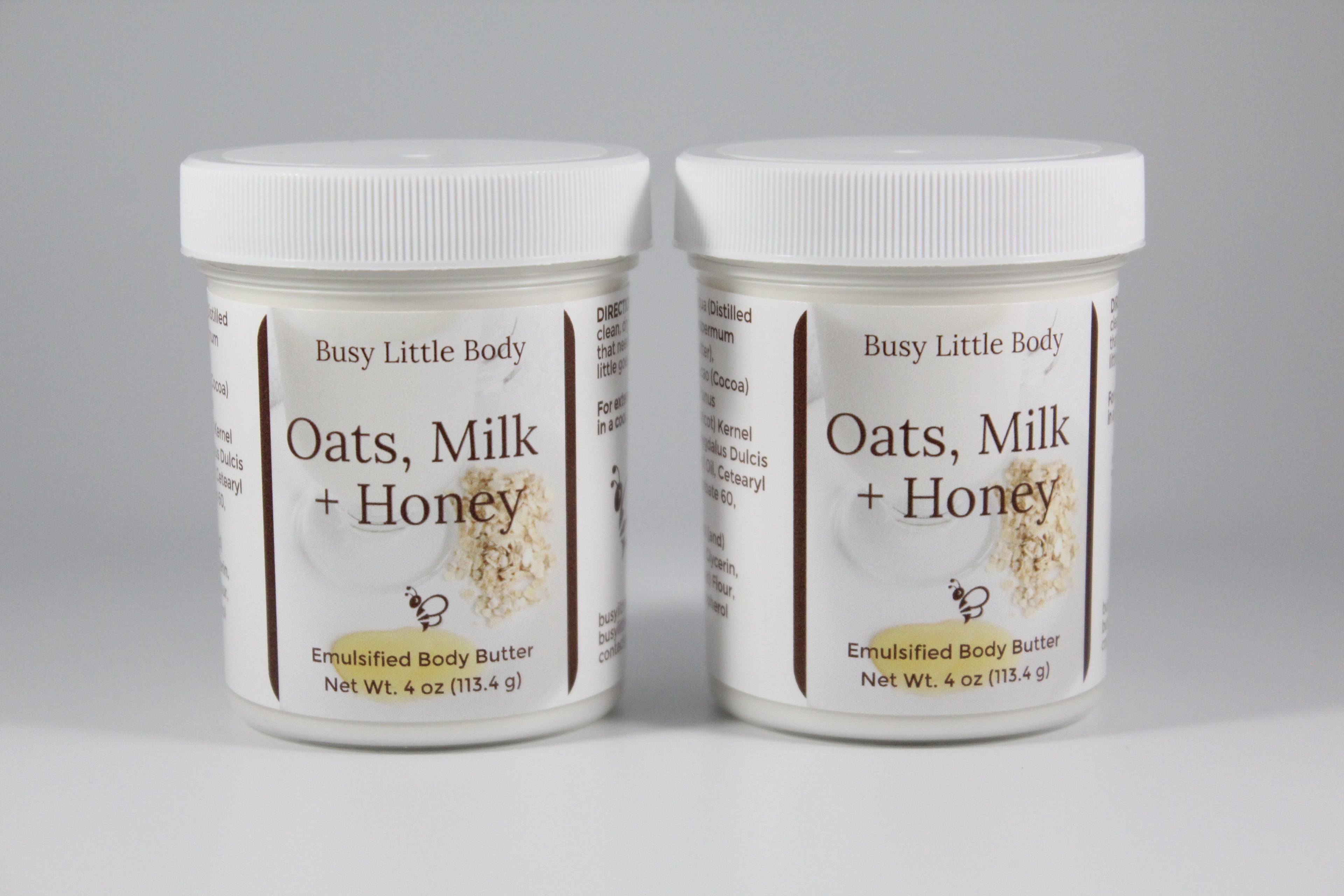 Two jars of 'Oats, Milk + Honey' body butter by Busy Little Body on a gray background