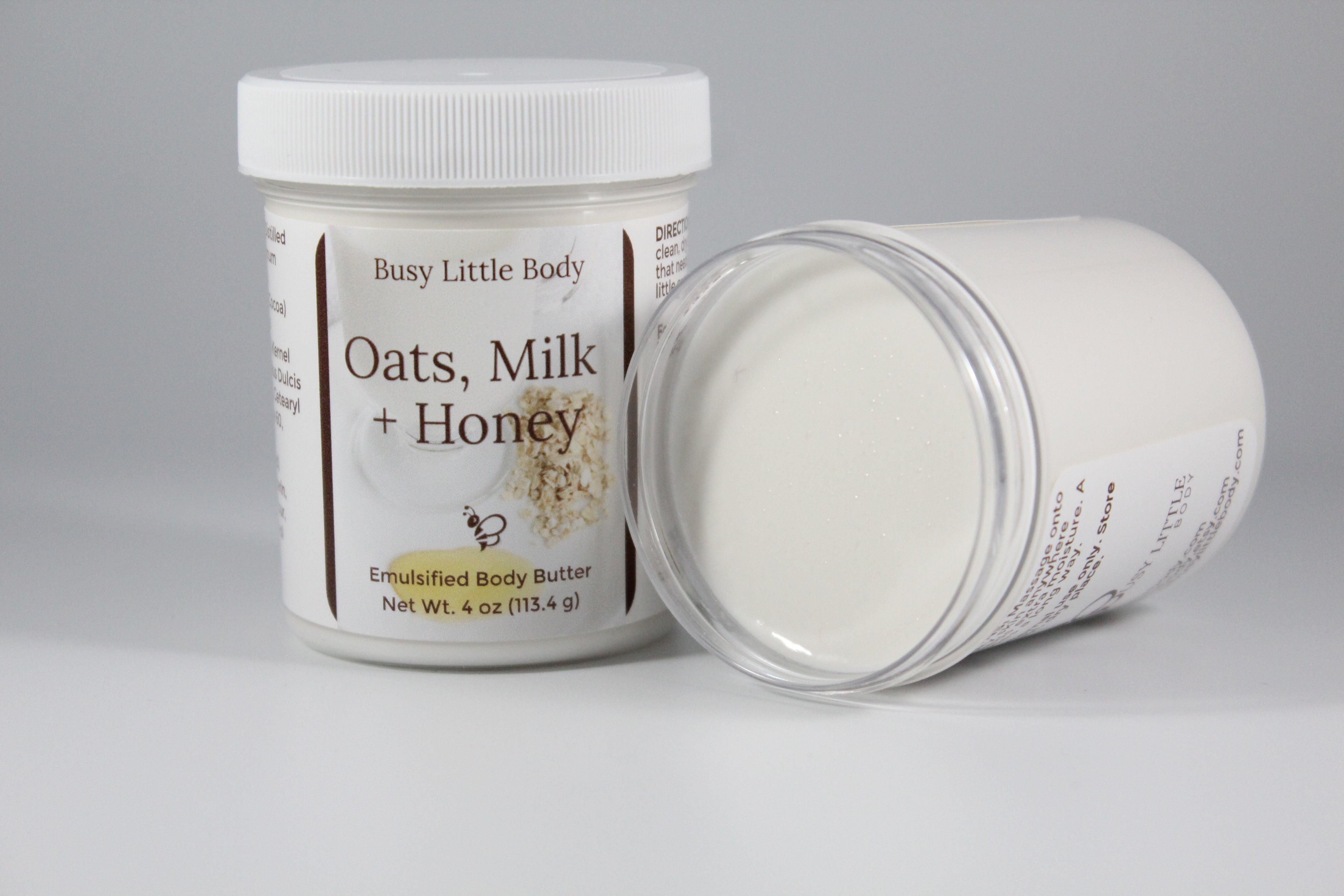 Two containers of 'Oats, Milk + Honey' emulsified body butter by Busy Little Body on a gray background.