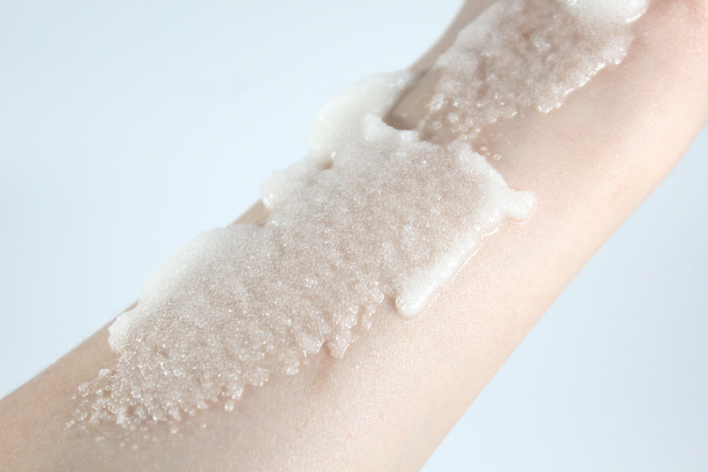 Close-up of a hand with a white sugar scrub swatch on a light background