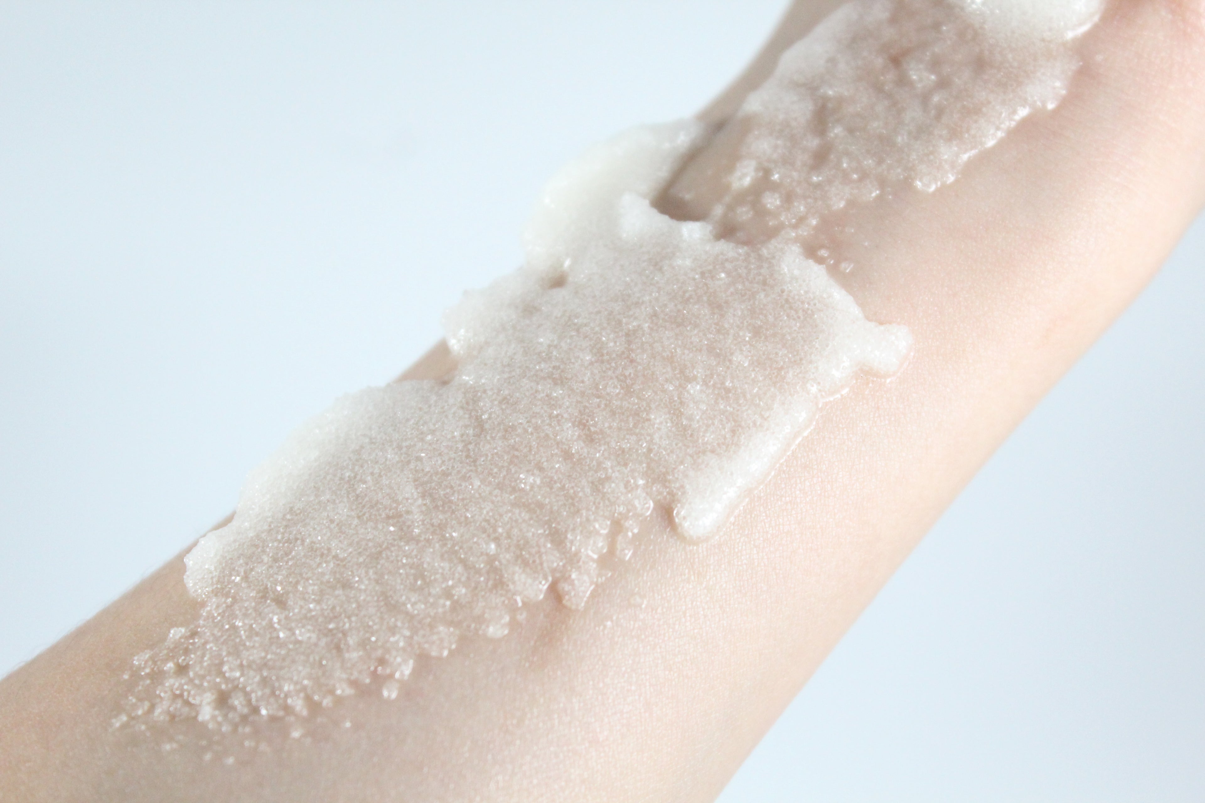 Close-up of a hand with a white sugar scrub swatch on a light background
