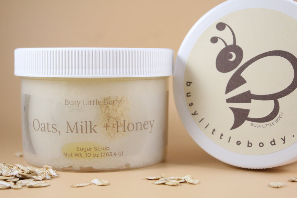 Two containers of 'Oats, Milk + Honey' sugar scrub with visible branding on a beige background.
