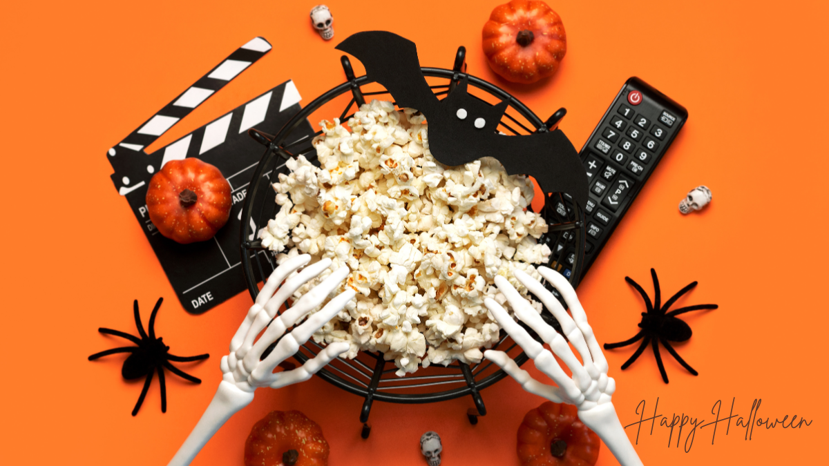 Orange background with skeleton hands reaching into a bowl of popcorn with tv remote, spiders, bat, and decorations.